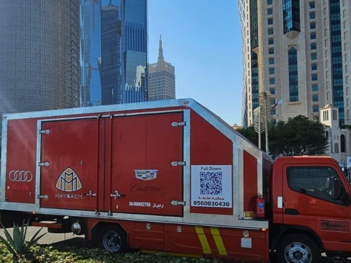 سطحة نقل سيارات (شاحنة مغلقة حمراء) تابعة لسطحات البدر السريع في الدوحة، قطر، لنقل السيارات الفاخرة (أودي، مايباخ، كاديلاك) بين المدن والشحن لدول الخليج